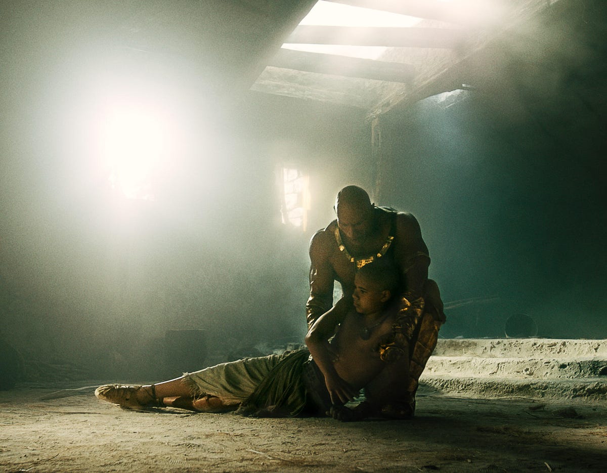 In a shadowy tomb, Dwayne Johnson cradles his son in the superhero movie Black Adam.