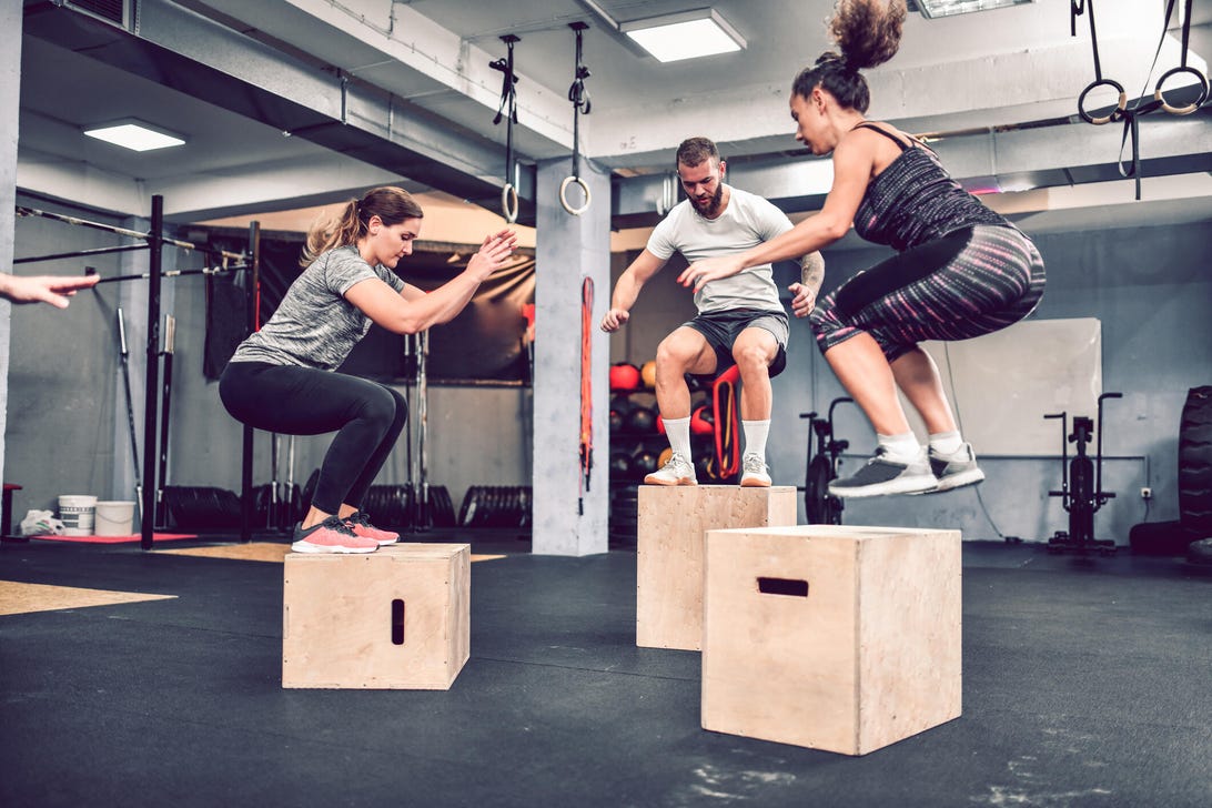 three people in a group fitness class do box jumps