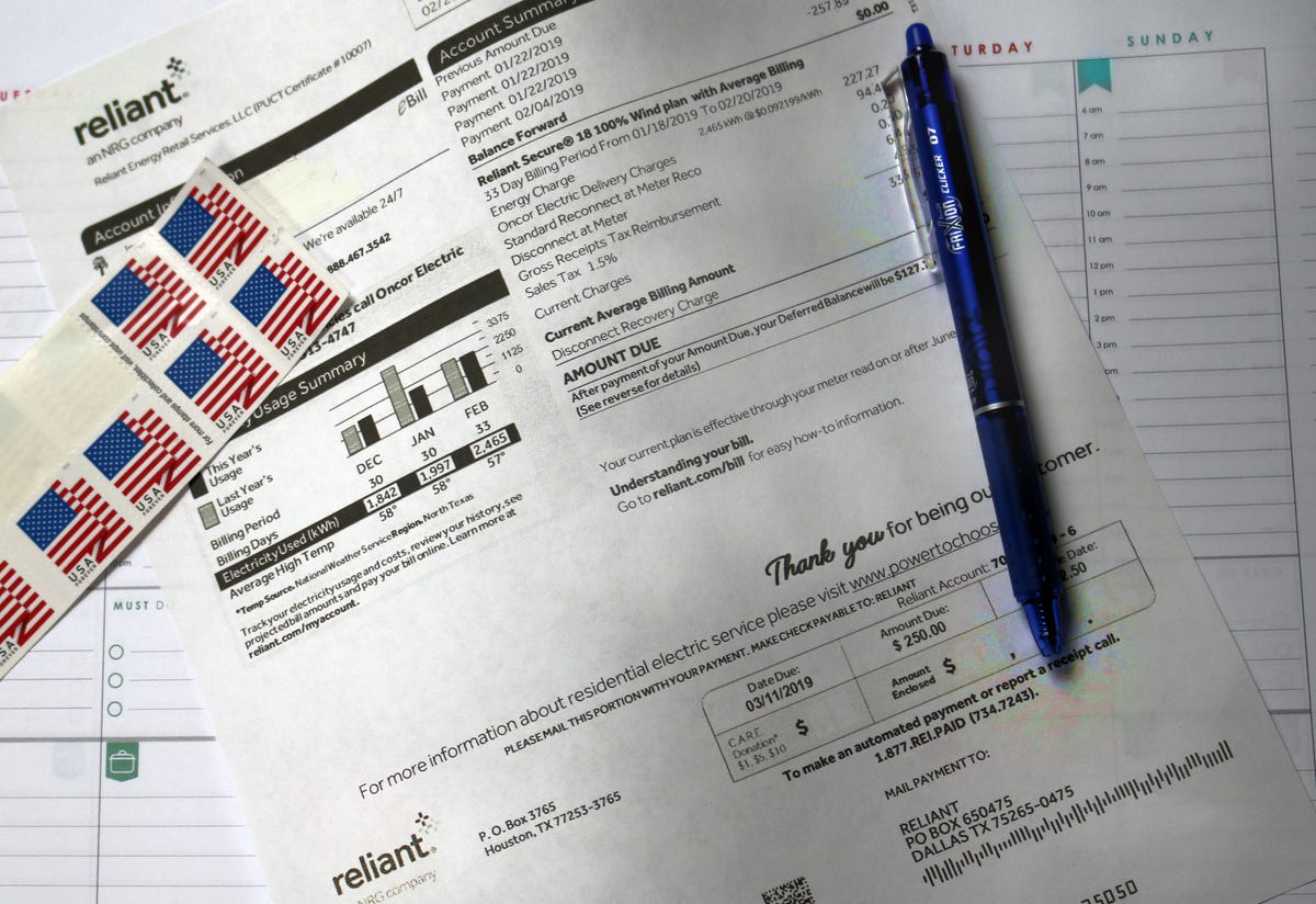 An electric utility bill, blue pen and American flag stamps.