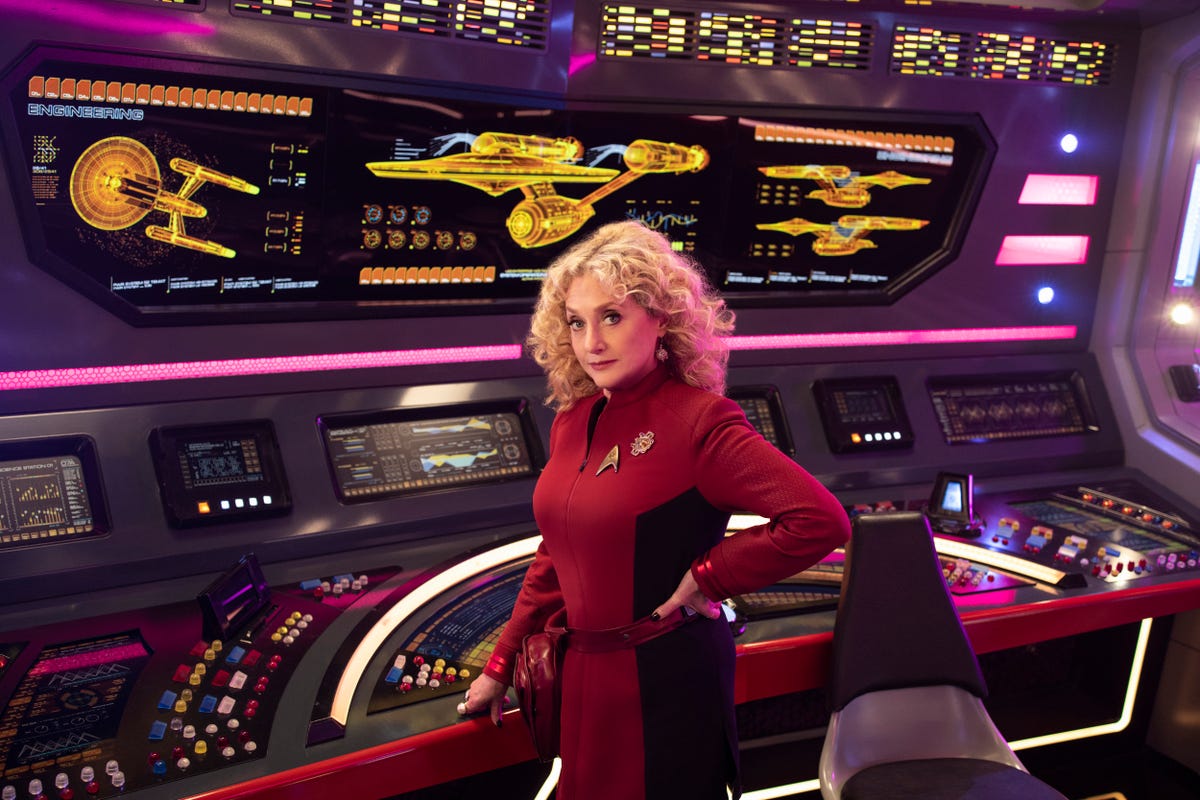 Carol Kane in red Starfleet uniform poses on the bridge of the Starship Enterprise.