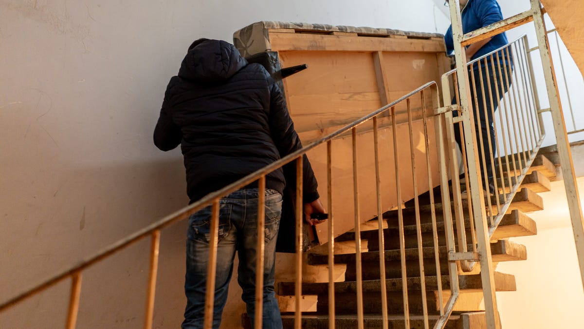 two people carry a heavy piece of furniture down a narrow stairwell