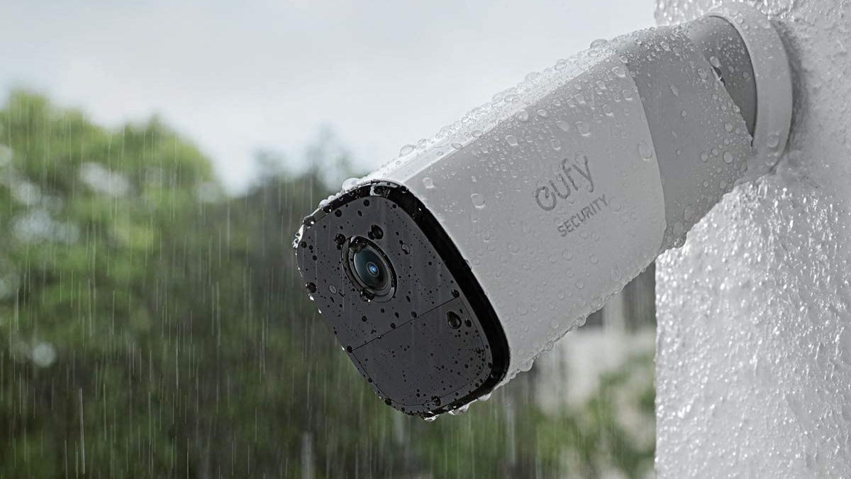 A white Eufy security camera mounted on an outdoor wall in the rain.