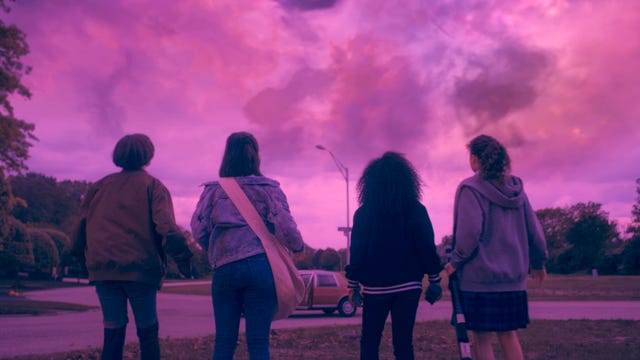 The backs of four young girls looking up at the sky, which has turned pink