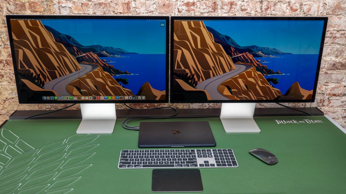 Portátil Apple MacBook Air M3 de 13 pulgadas conectado a dos pantallas Studio, sentado sobre una mesa verde.