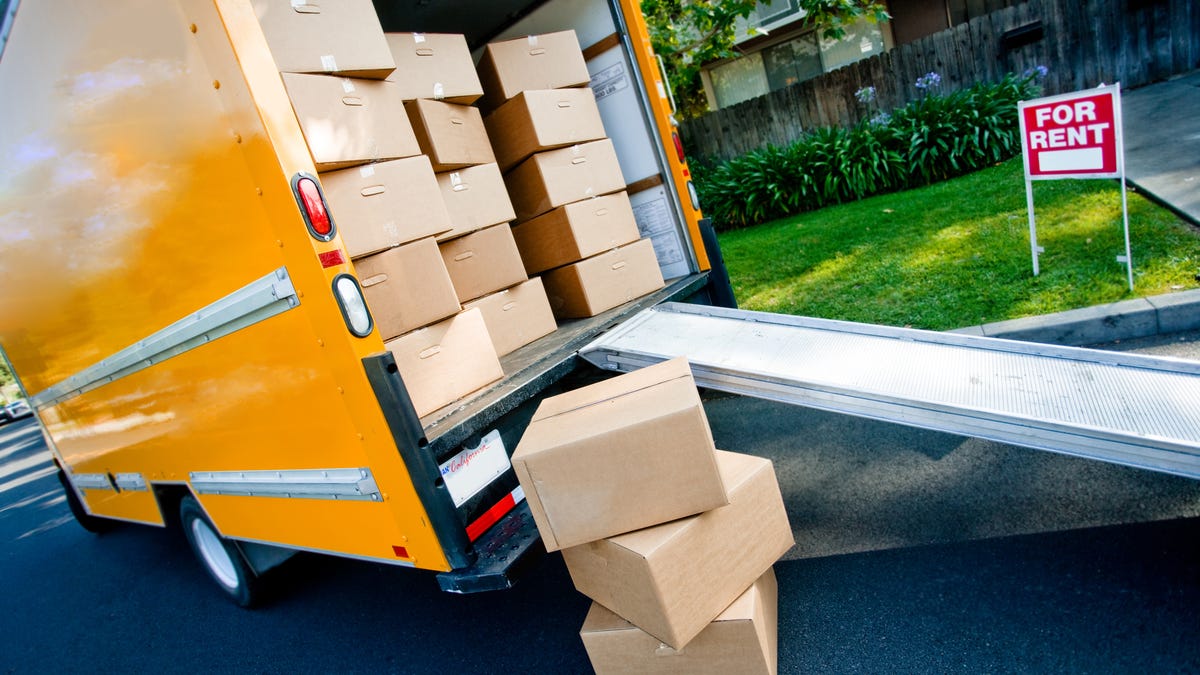 a yellow moving truck with a ramp out the back holds many cardboard boxes while some boxes sit on the ground behind the truck