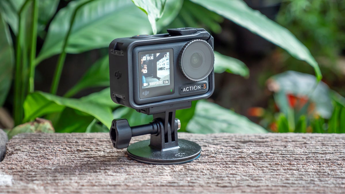 DJI Osmo Action 3 action camera attached to a mount on a wall with plants in the background.