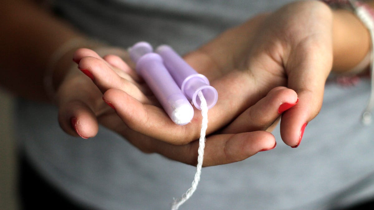 A woman holds a tampon with a purple applicator in her hands