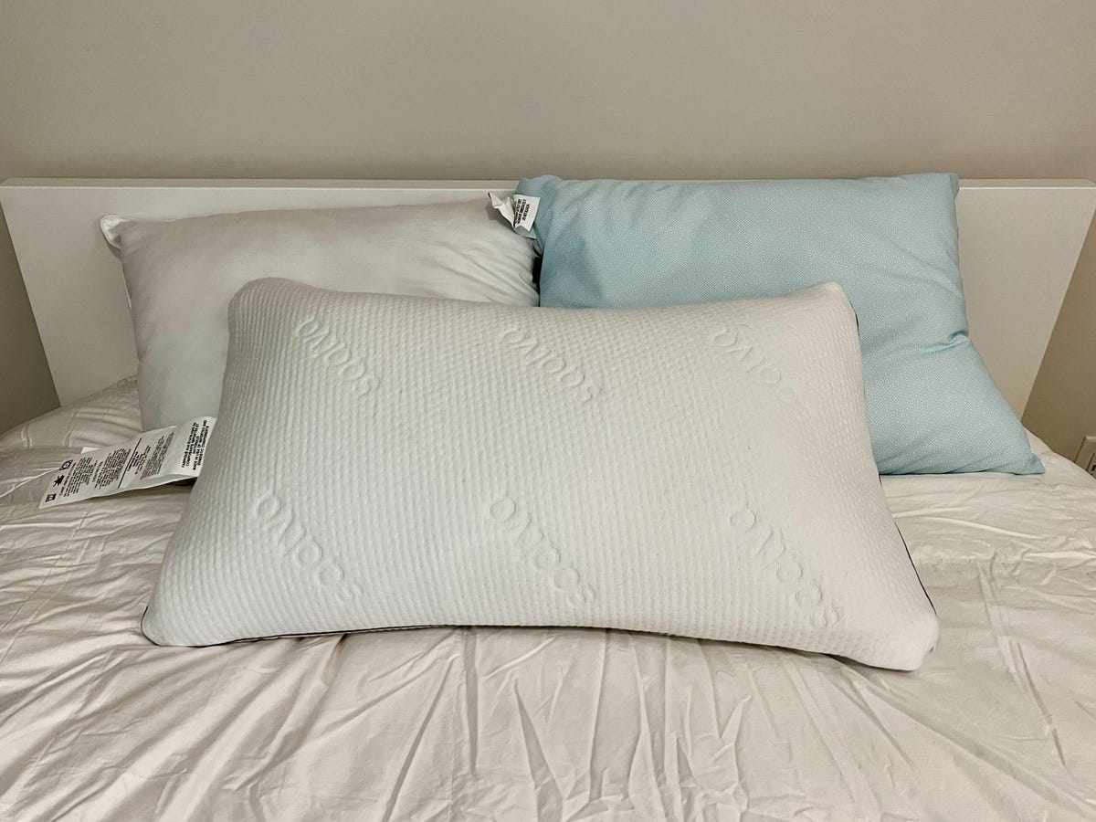 Saatva Graphite Memory Foam Pillow, Slumber Cloud UltraCool, and Parachute Down Alternative pillow on a white bed.