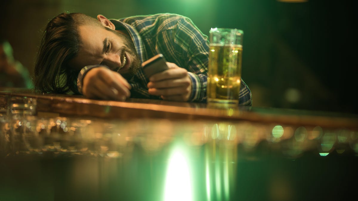 Young wasted man text messaging on cell phone while leaning on a bar counter.