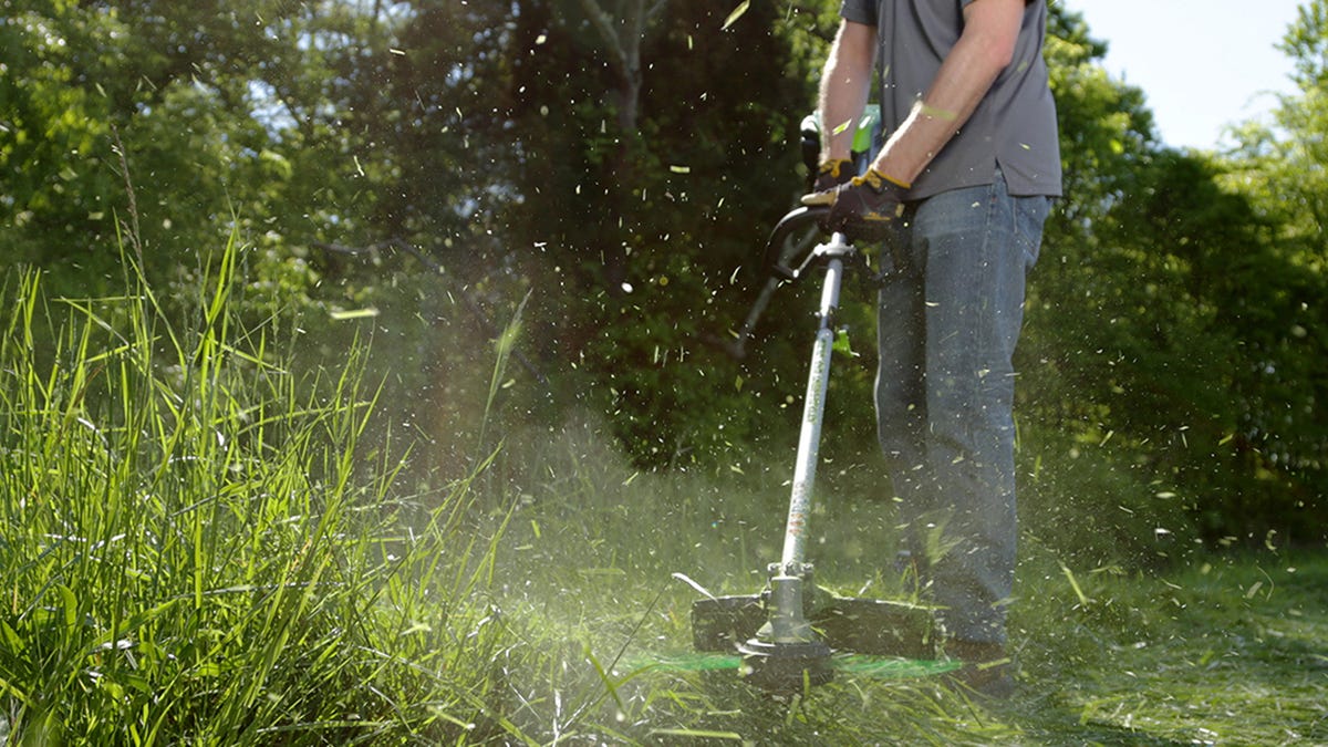 A man cuts through tall grass with a 16-inch string trimmer from Greenworks.