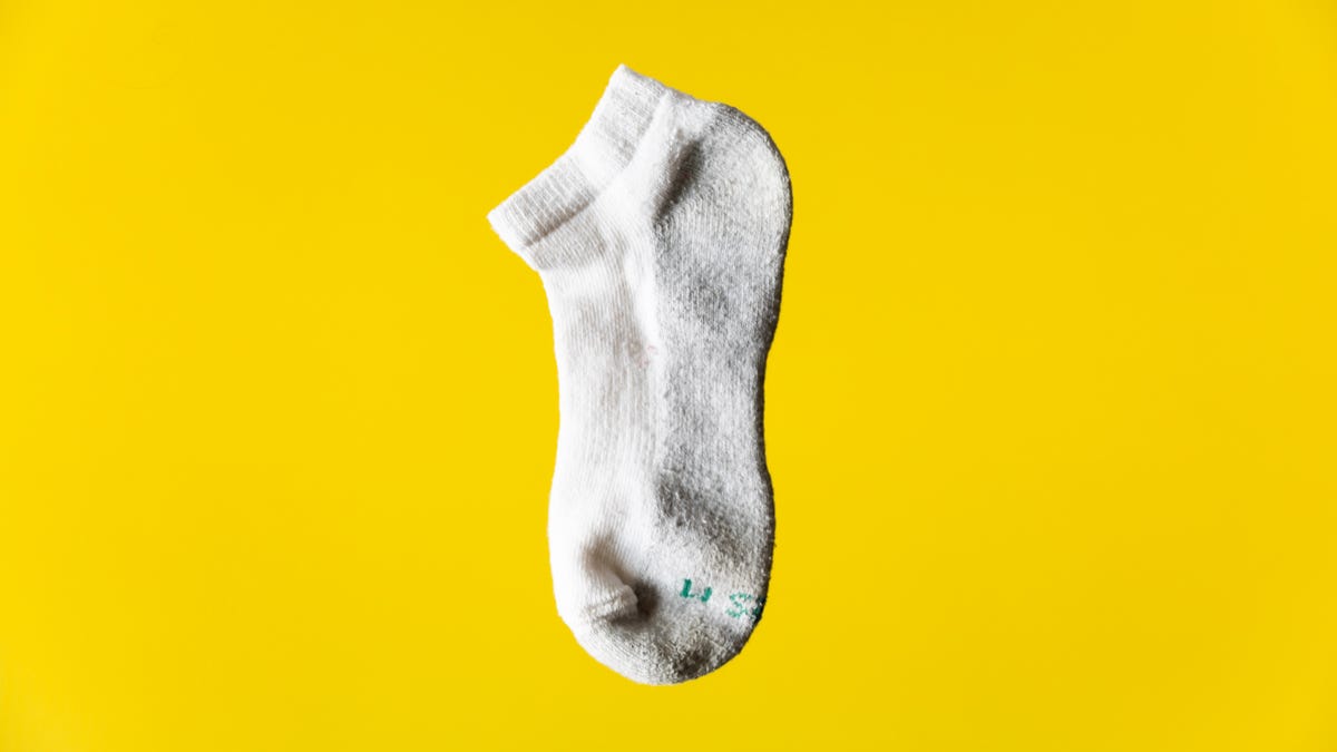 A single white ankle sock on a yellow background.