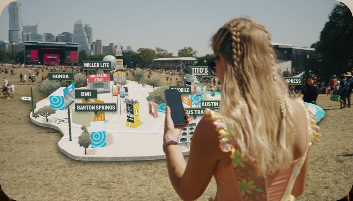 A person holding a phone up at an outdoor event, while a visual simulation of a map appears in front of them