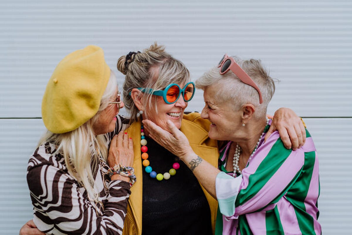 Três mulheres mais velhas felizes vestindo roupas coloridas.