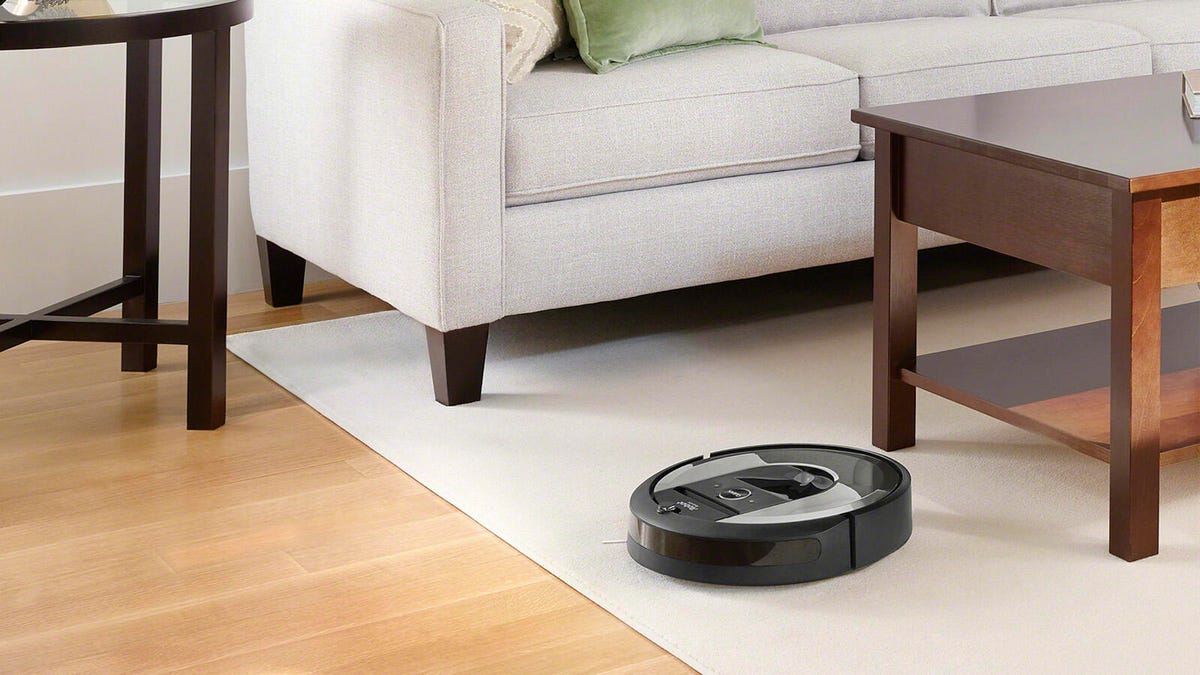 The iRobot Roomba i6 navigates across a rug near a sofa and coffee table.