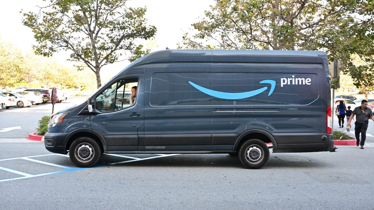 A blue Amazon delivery van with the Prime logo on the side is seen in at a crosswalk.