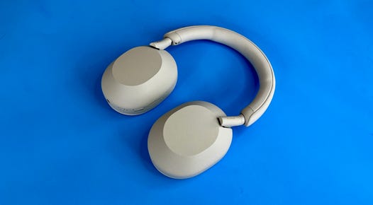 A pair of white Sony WH-1000XM5 headphones against a blue background