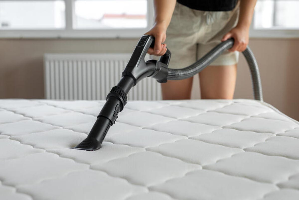 Person cleaning a mattress with a vacuum handle attachment.