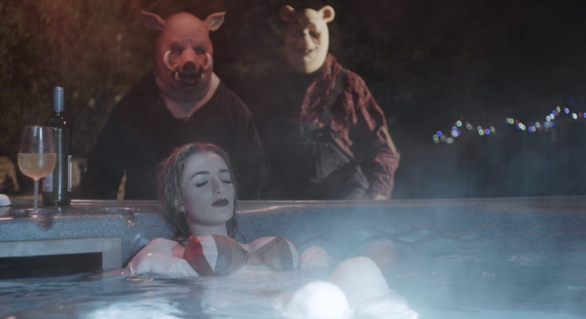 Scary figures wearing piglet and bear masks creep up on a woman in a hot tub.