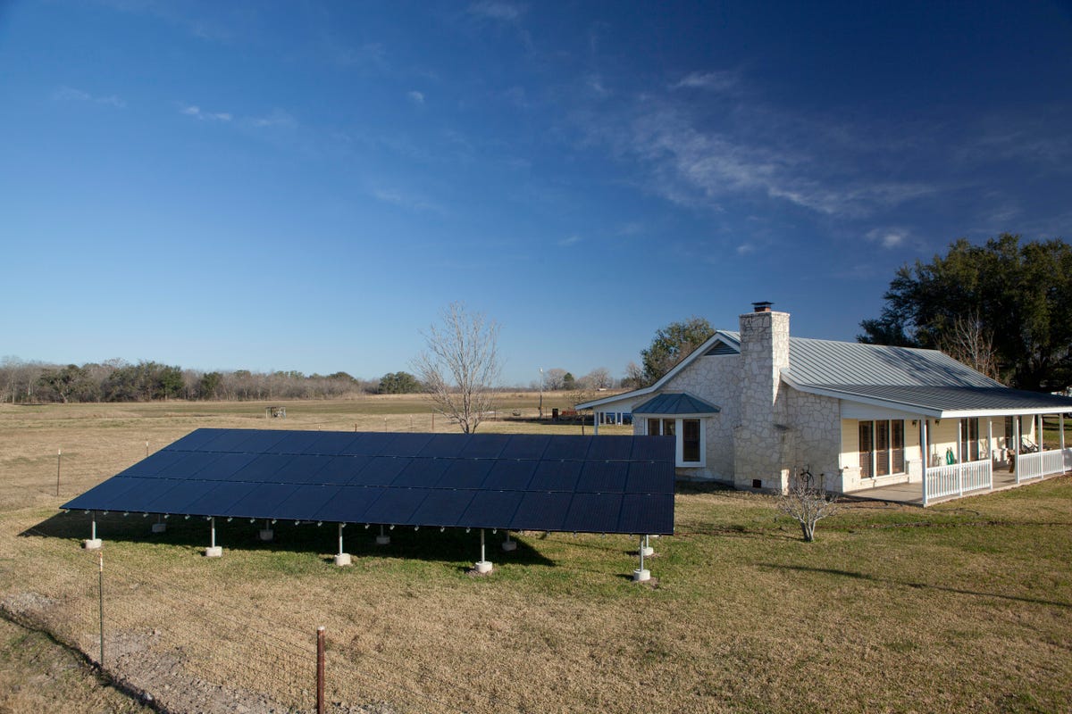 Solar panels mounted beside a house in a rural setting.