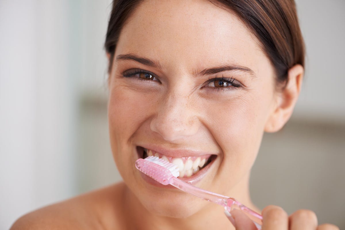 woman brushing teeth with pink toothbrush