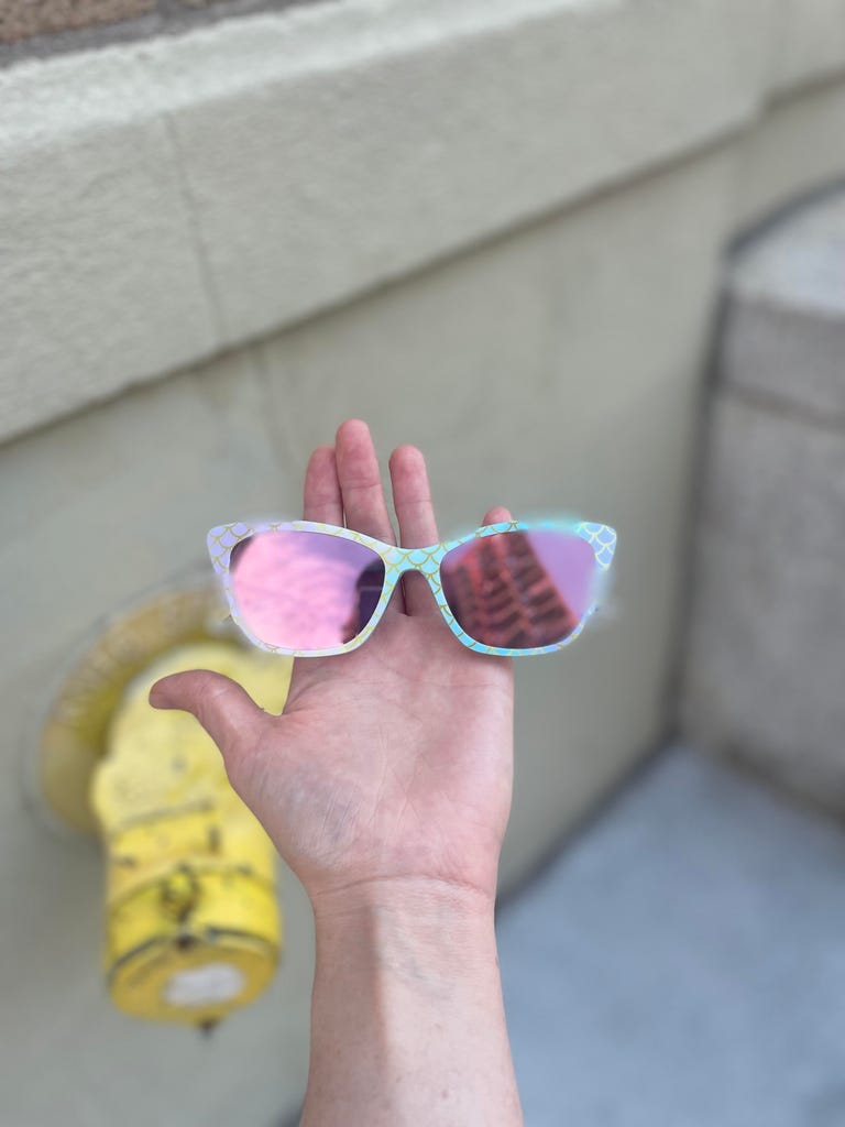 A pair of sunglasses held out on a hand against a pavement background