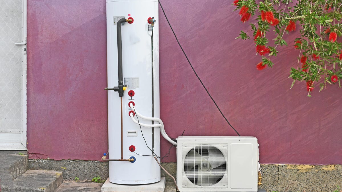 A heat pump water heater against a maroon exterior wall.