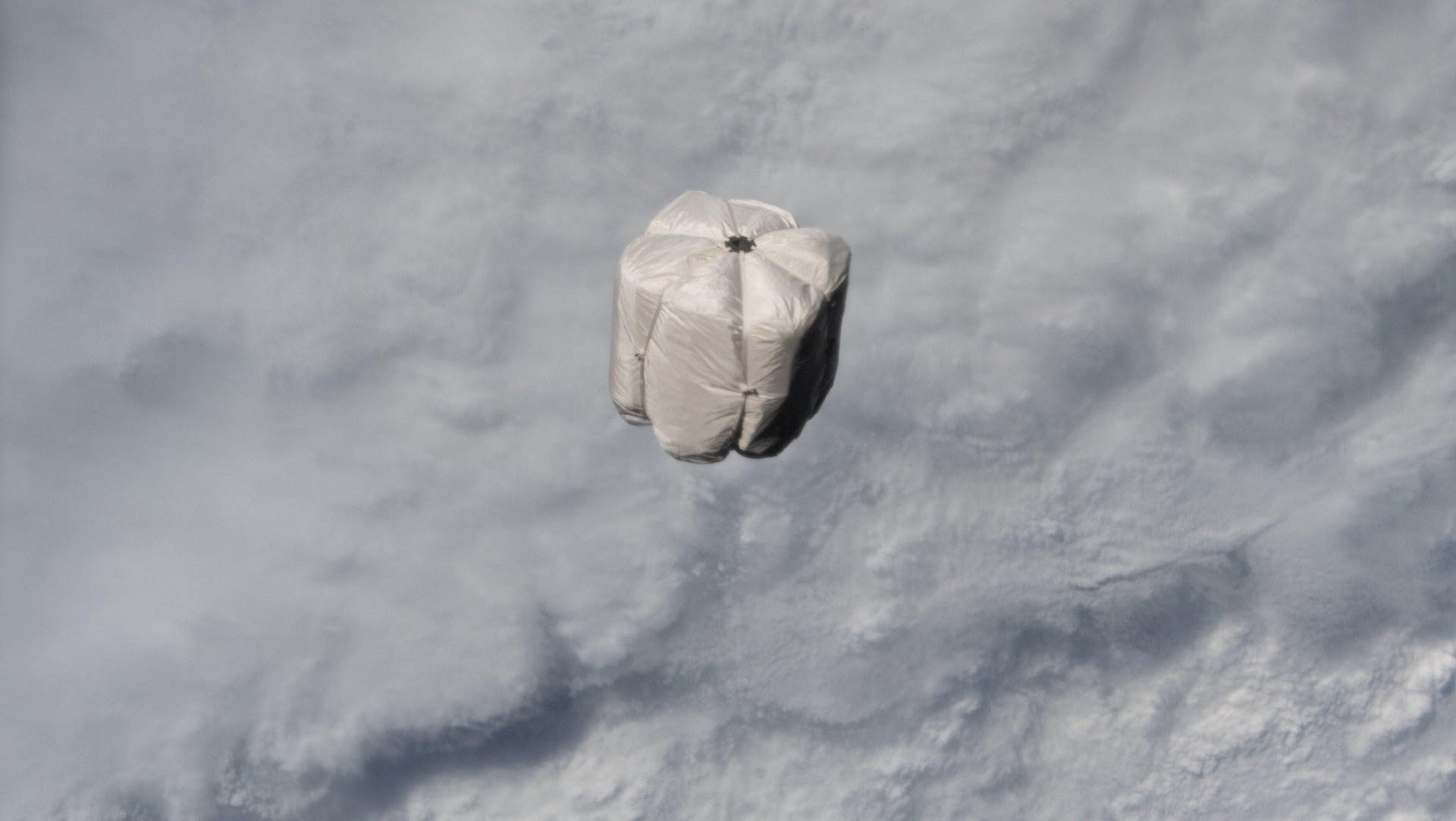 A trash bag floats in orbit above the clouds of Earth.