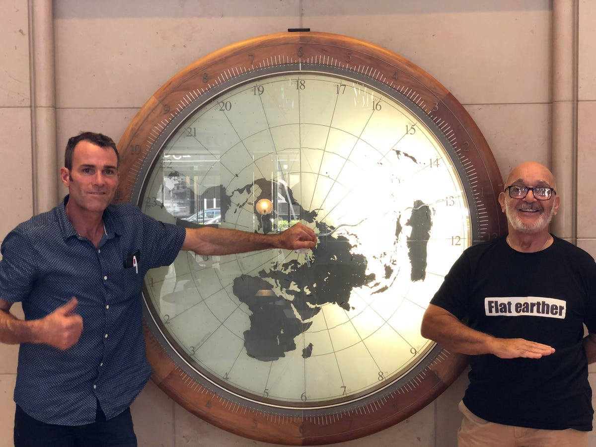 Lee and Artigas, the two people who turned up to the flat-Earth convention, in front of a map of the world.