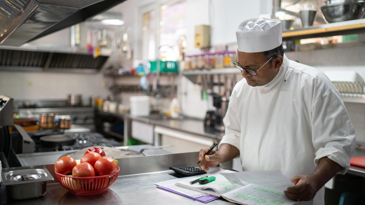 A chef working on the kitchen finances while standing at a counter in a commercial kitchen