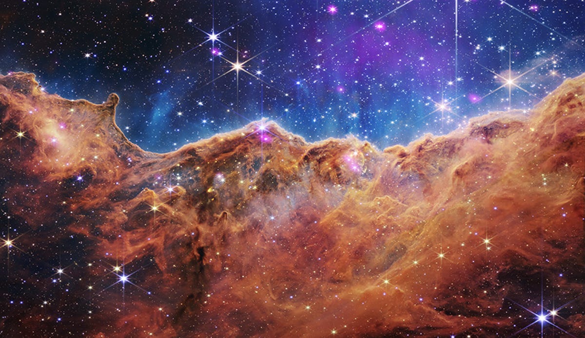 The rocks of the Carina Nebula appear brownish-brown, and the upper part of the image is blue.  Stars are dotted everywhere.