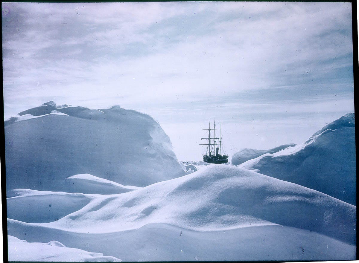 The ship Endurance is visible in the distance among mountains of snow and ice formed over the sea