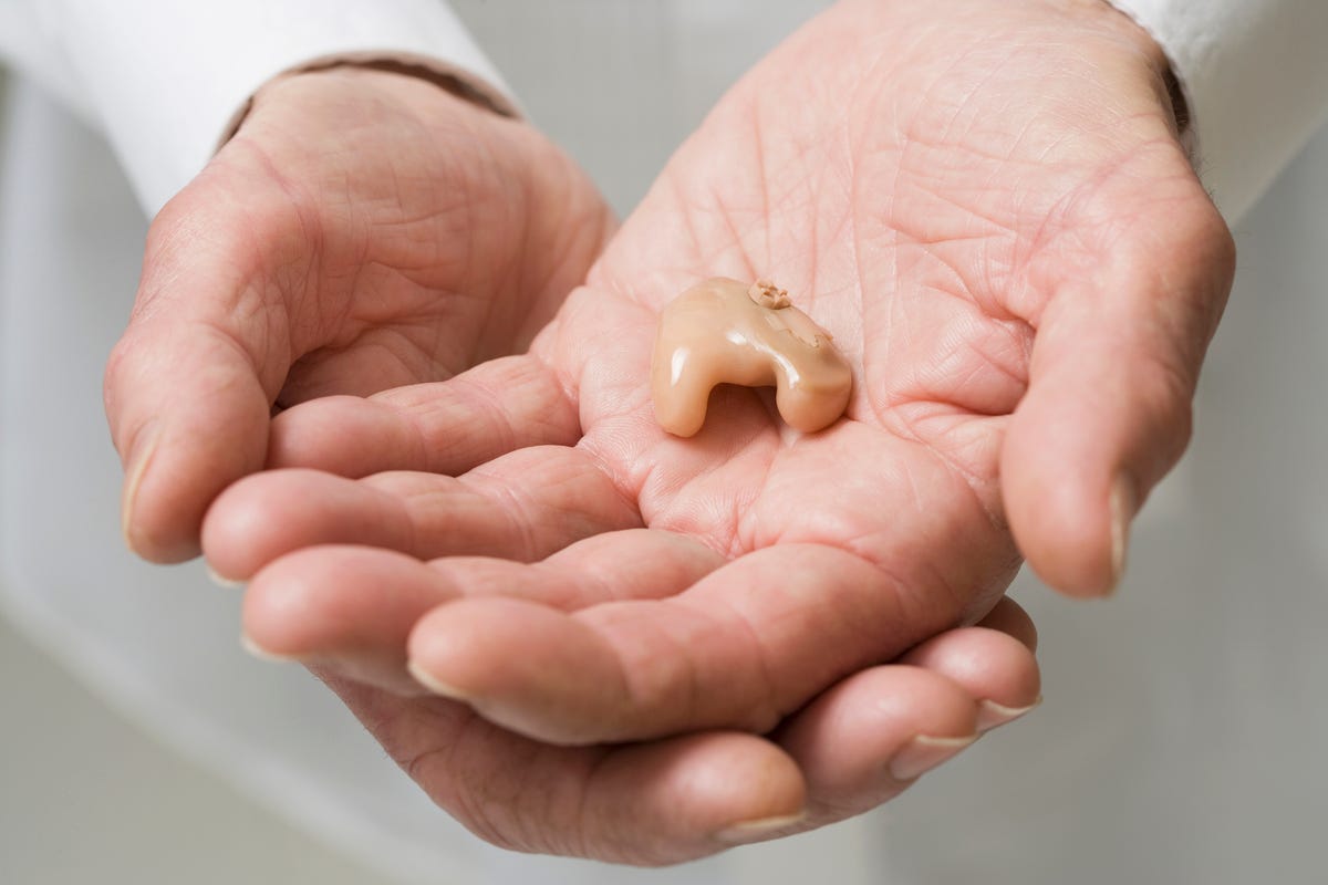 Hands holding an in-ear hearing aid
