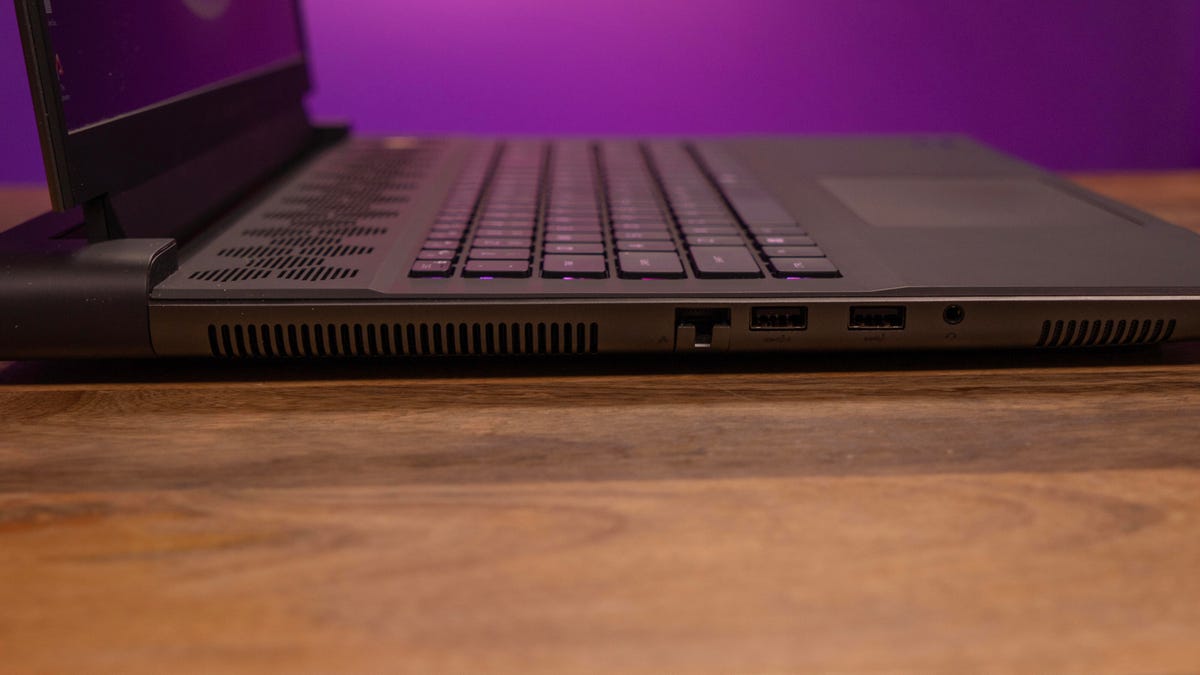 Alienware m18 R2 open, showing the left side with the vents, Ethernet, two USB-A and combo audio ports, on a wood table with a magenta and purple background