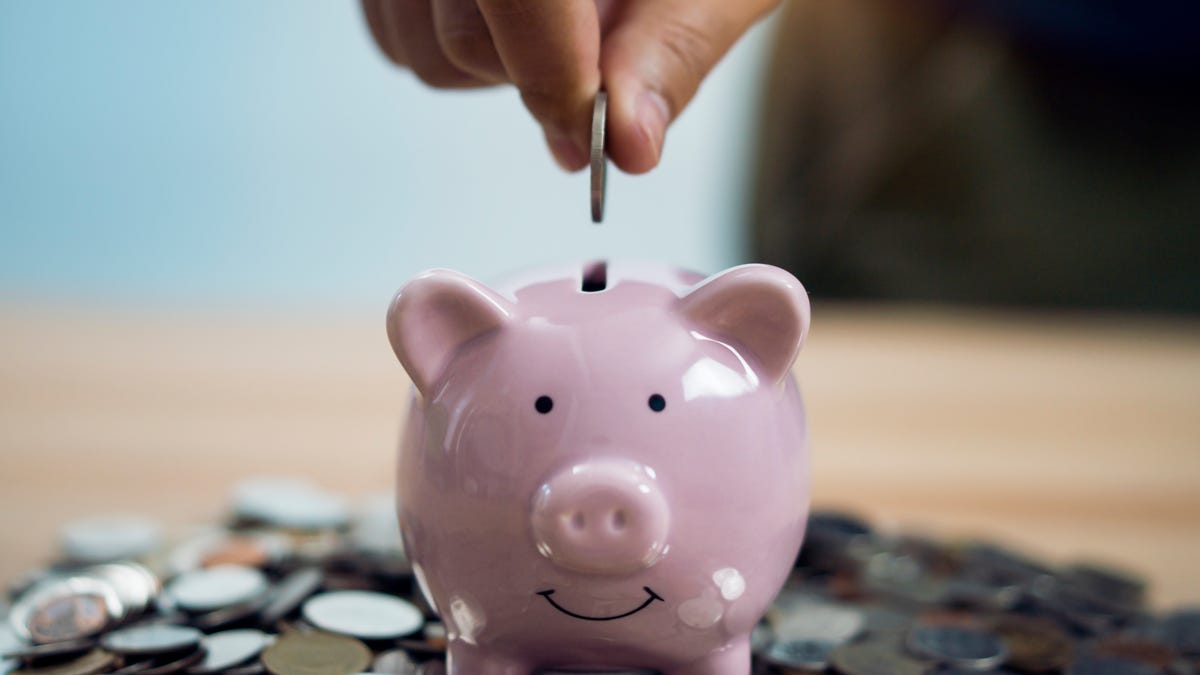 Person making a coin deposit in a piggy bank that is sitting on a pile of coin-like objects