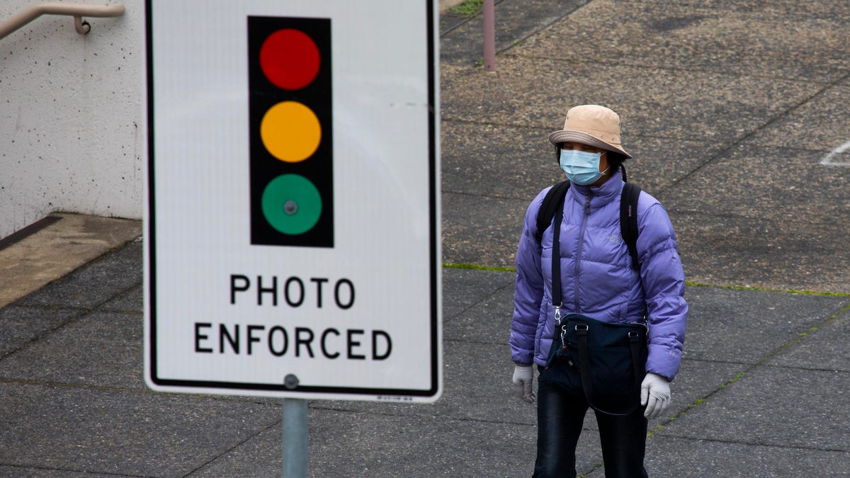 Person wearing a face mask next to a stoplight sign that reads "photo enforced"