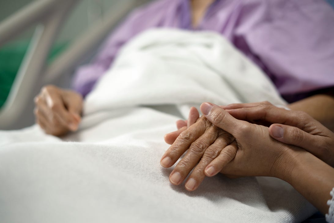 Patient in a hospital bed holding someone's hand.