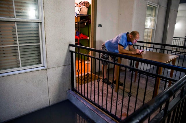 A Houston resident checks his phone as flood waters rise near his door.