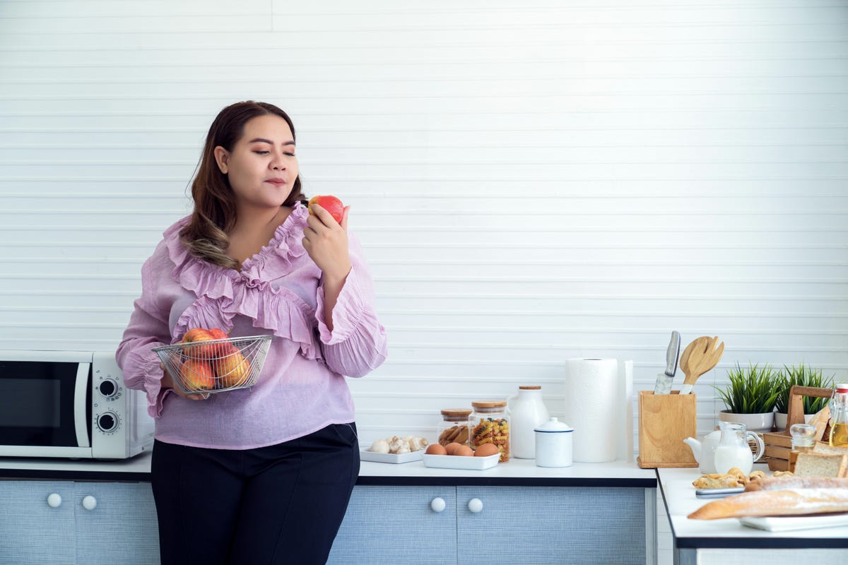 Woman stands in kitchen eating fresh fruit