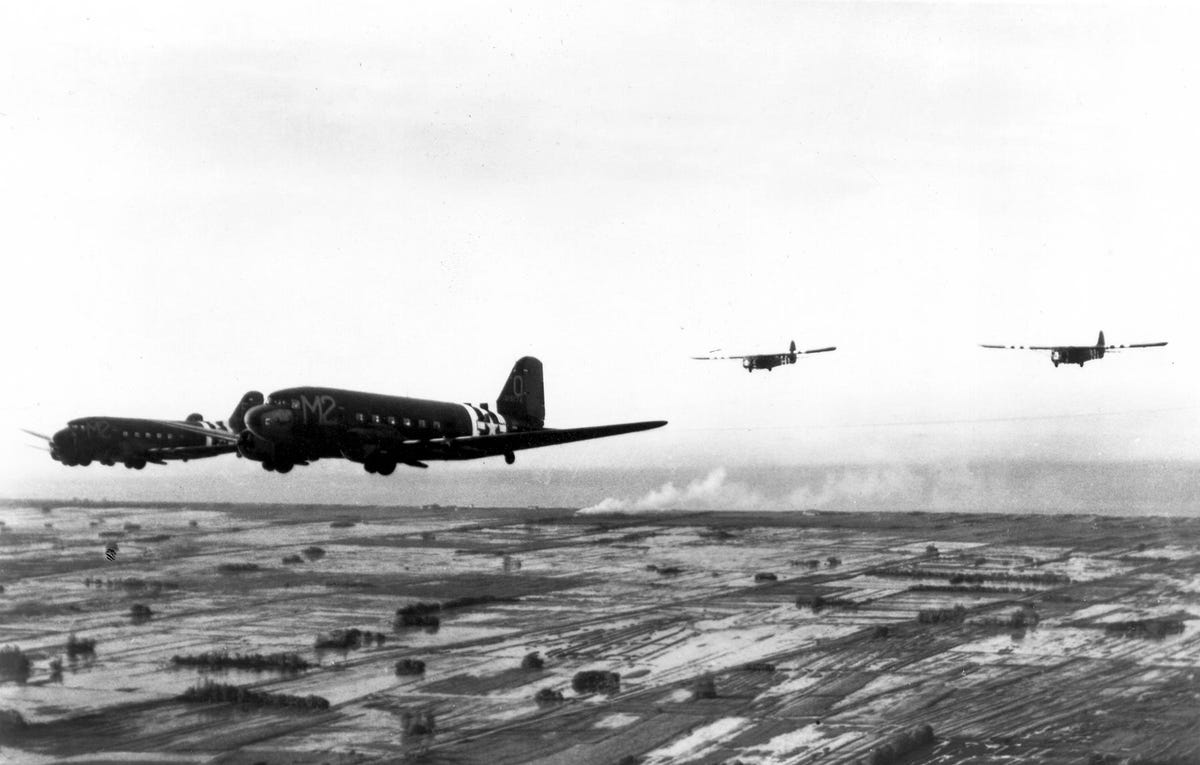 A pair of Douglas C-47 Skytrain aircraft towing Waco gliders over a Normandy beach