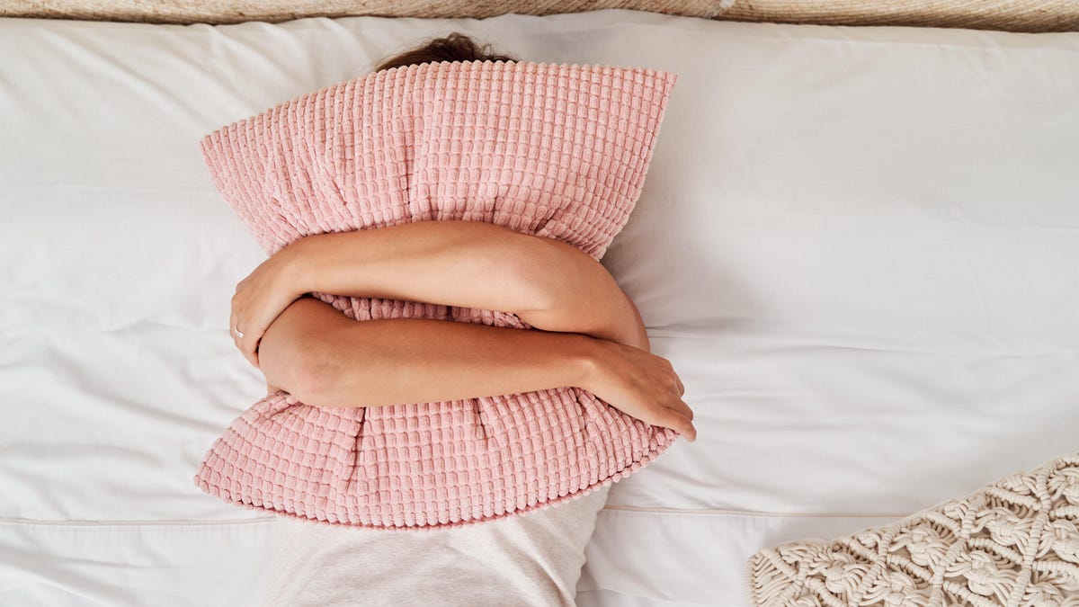 Person hugging pillow in bed, covering face.