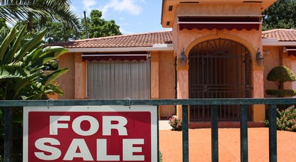A stucco house with a for sale sign on a wrought iron gate