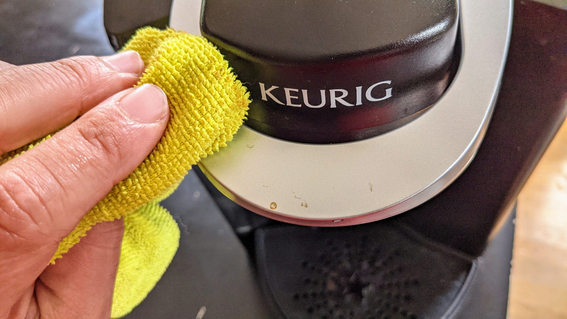 A hand wiping the handle of a Keurig with a cloth