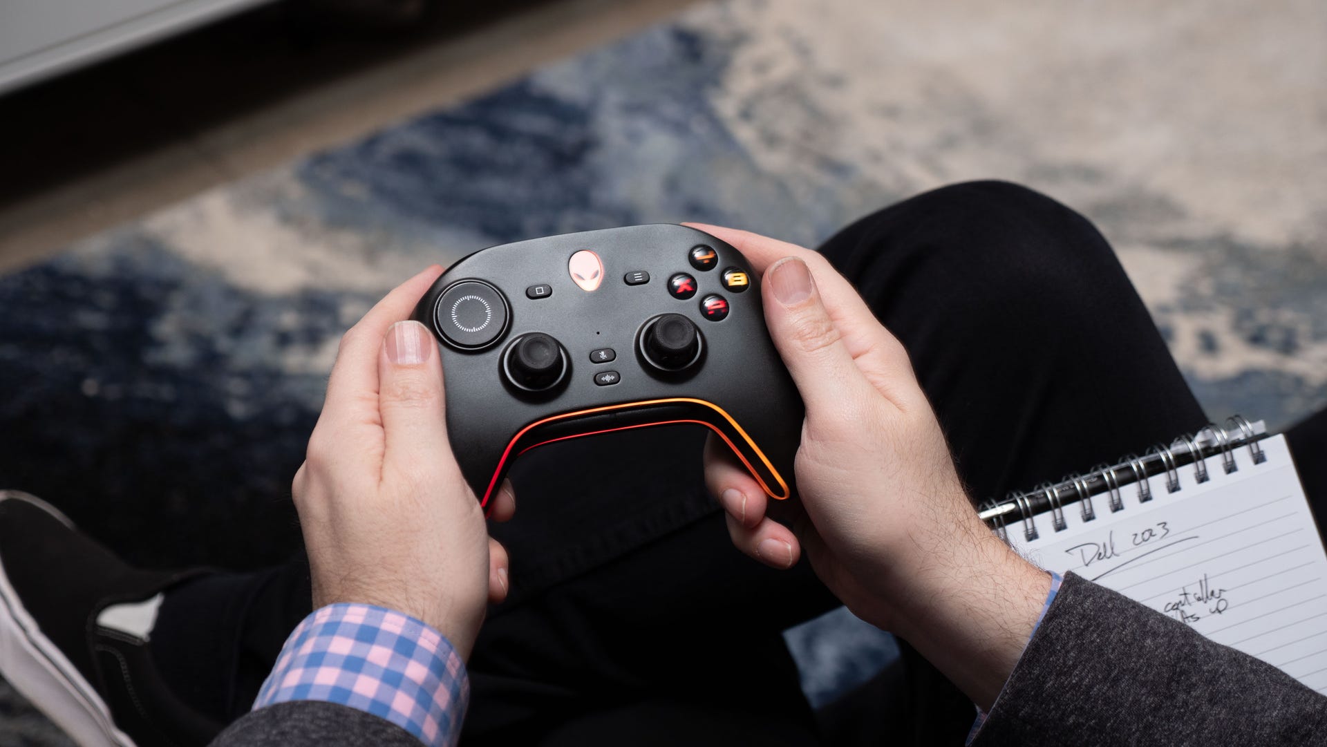 hands holding a black gaming controller with Dell's Alienware logo as the center button