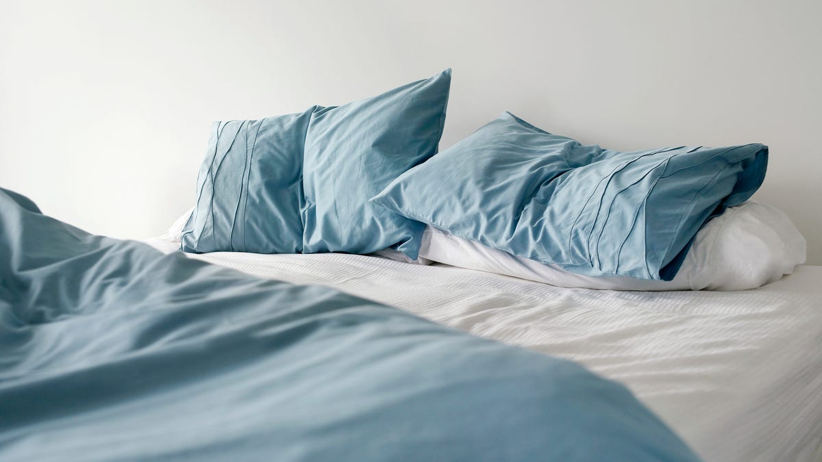 Blue-gray and white pillows on a bed with white sheets and a blue-gray comforter