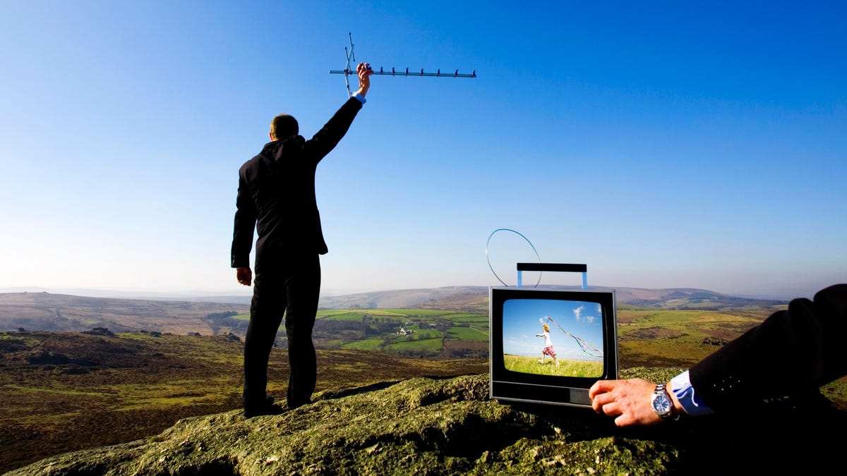 A man in a suit stands on a mountain while holding an antenna.