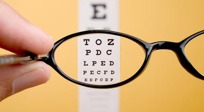 Pair of glasses being held in front of a Snellen Chart.