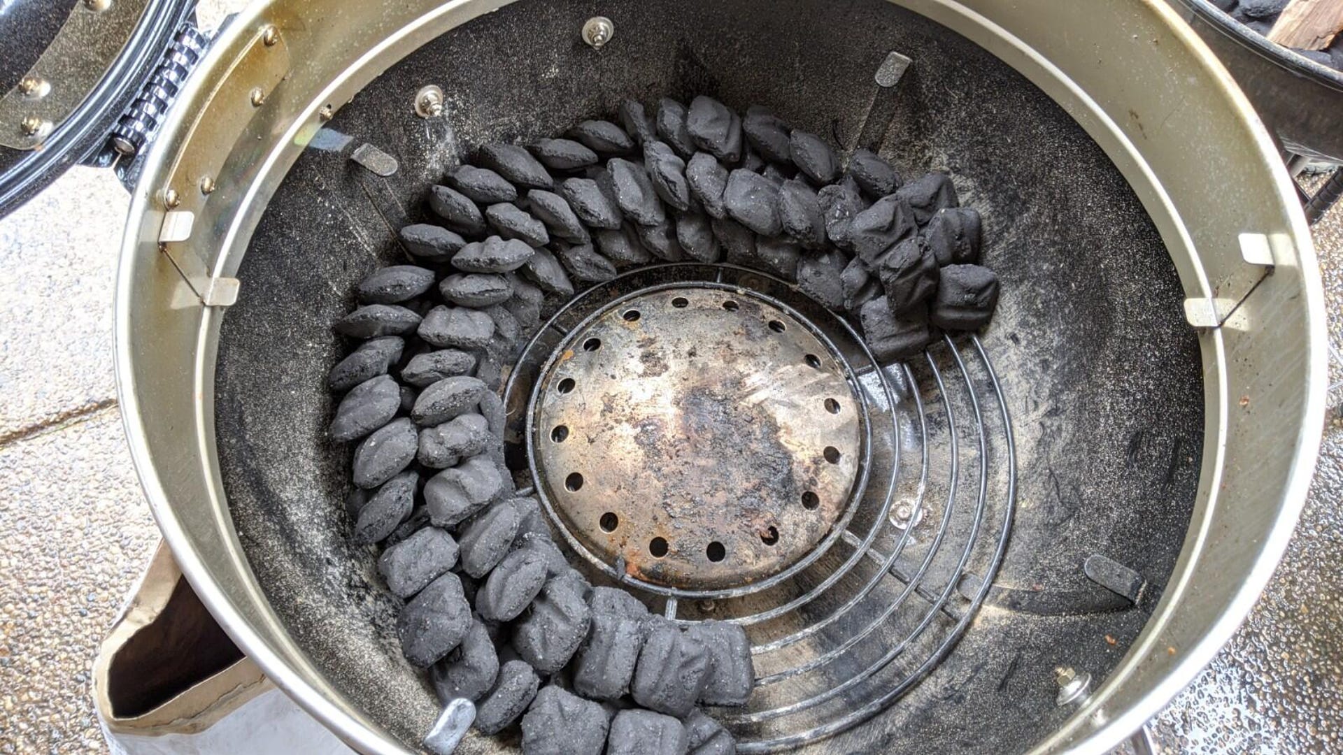 The interior of a round grill with two rows of briquettes stacked two thirds of the way around the center 