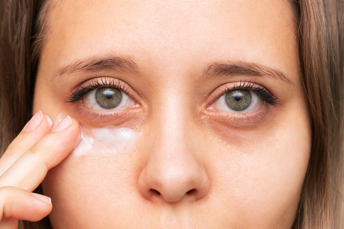 Close up of young woman applying eye cream on dark circles under eyes