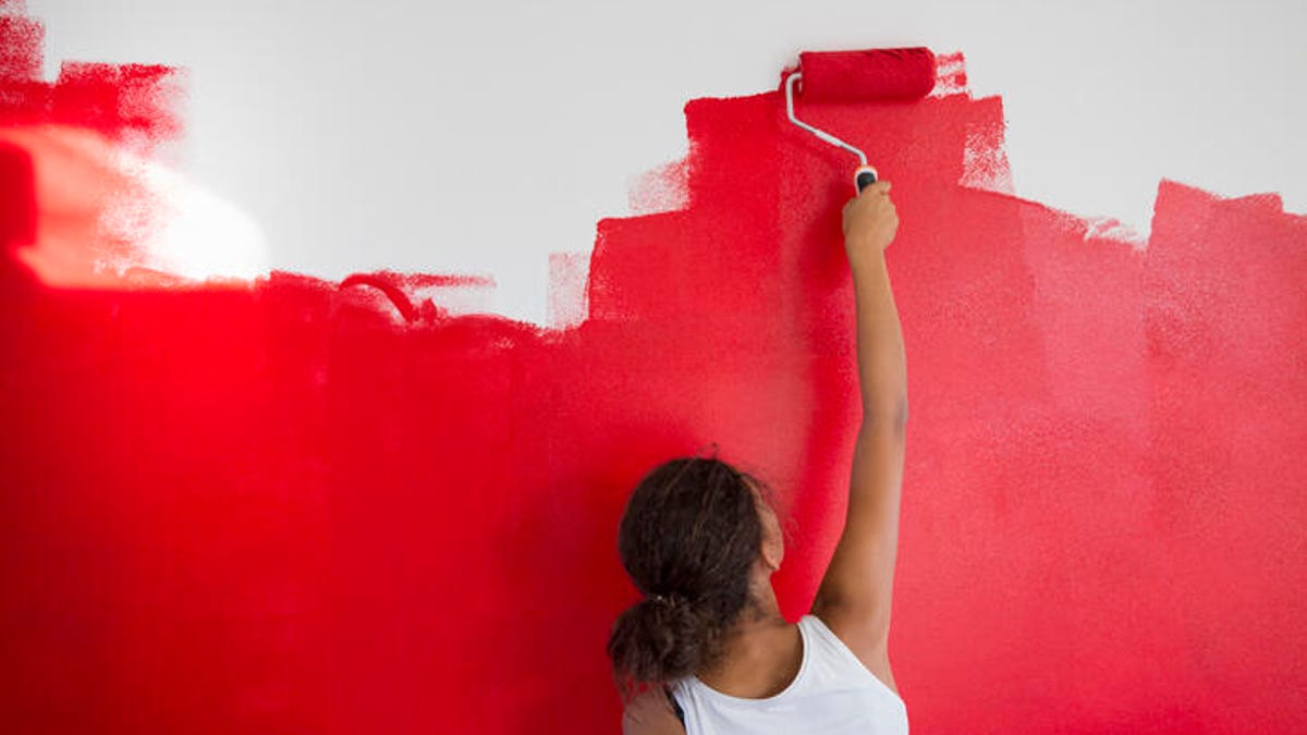 Woman painting a wall red with a roller brush