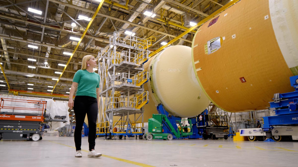 A woman stands next to the two large tanks that comprise the Artemis core stage, inside the Michoud Assembly Facility.